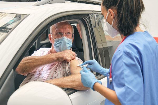 Crop medic preparing elderly patient for vaccination in car